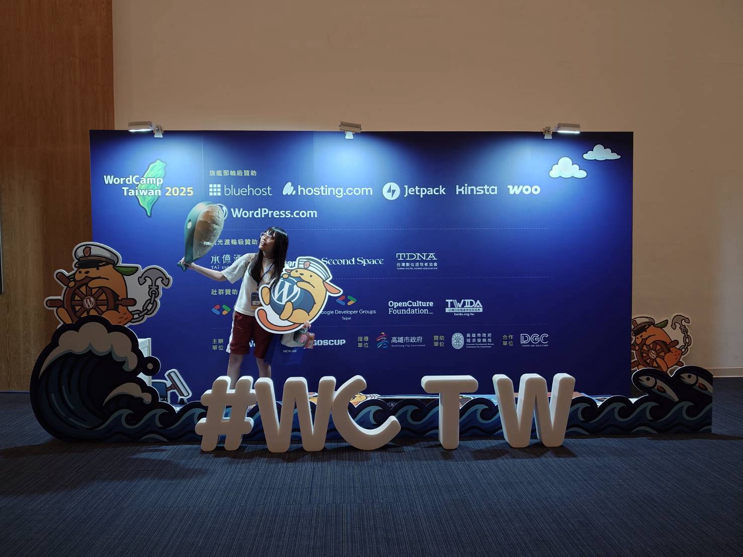 白白在 2025 WordCamp Taiwan 會場與 #WCTW 立牌合影