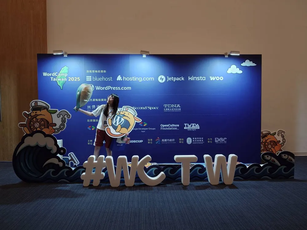 白白在 2025 WordCamp Taiwan 會場與 #WCTW 立牌合影